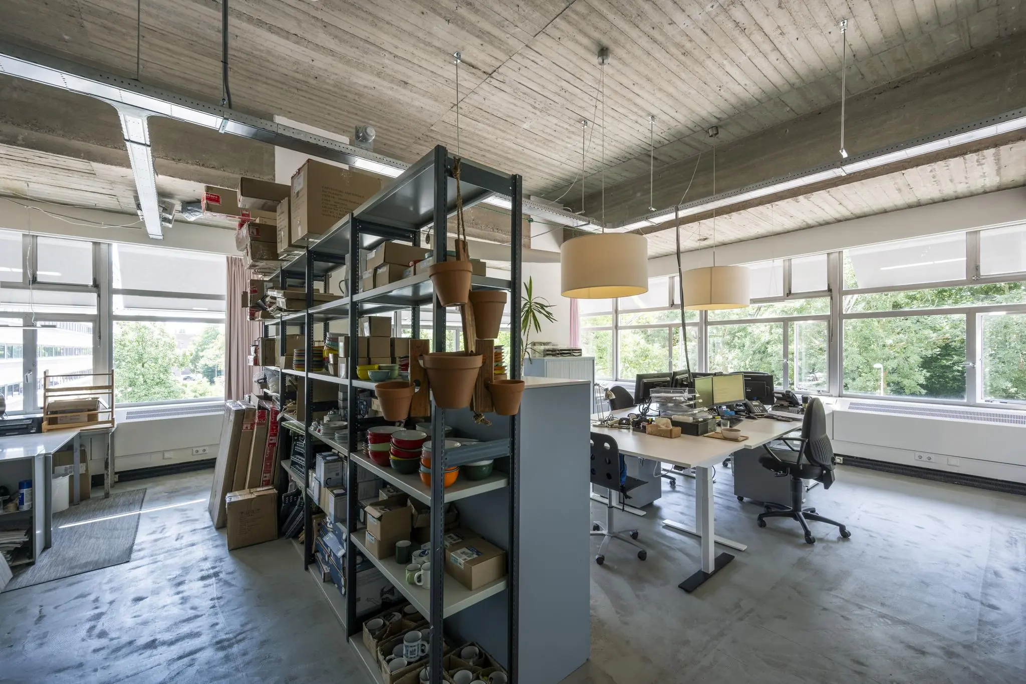 Modern kantoor met open werkplekken, grote ramen en een stellingkast vol kantoor- en keukenspullen aan de Van Leijenberghlaan.